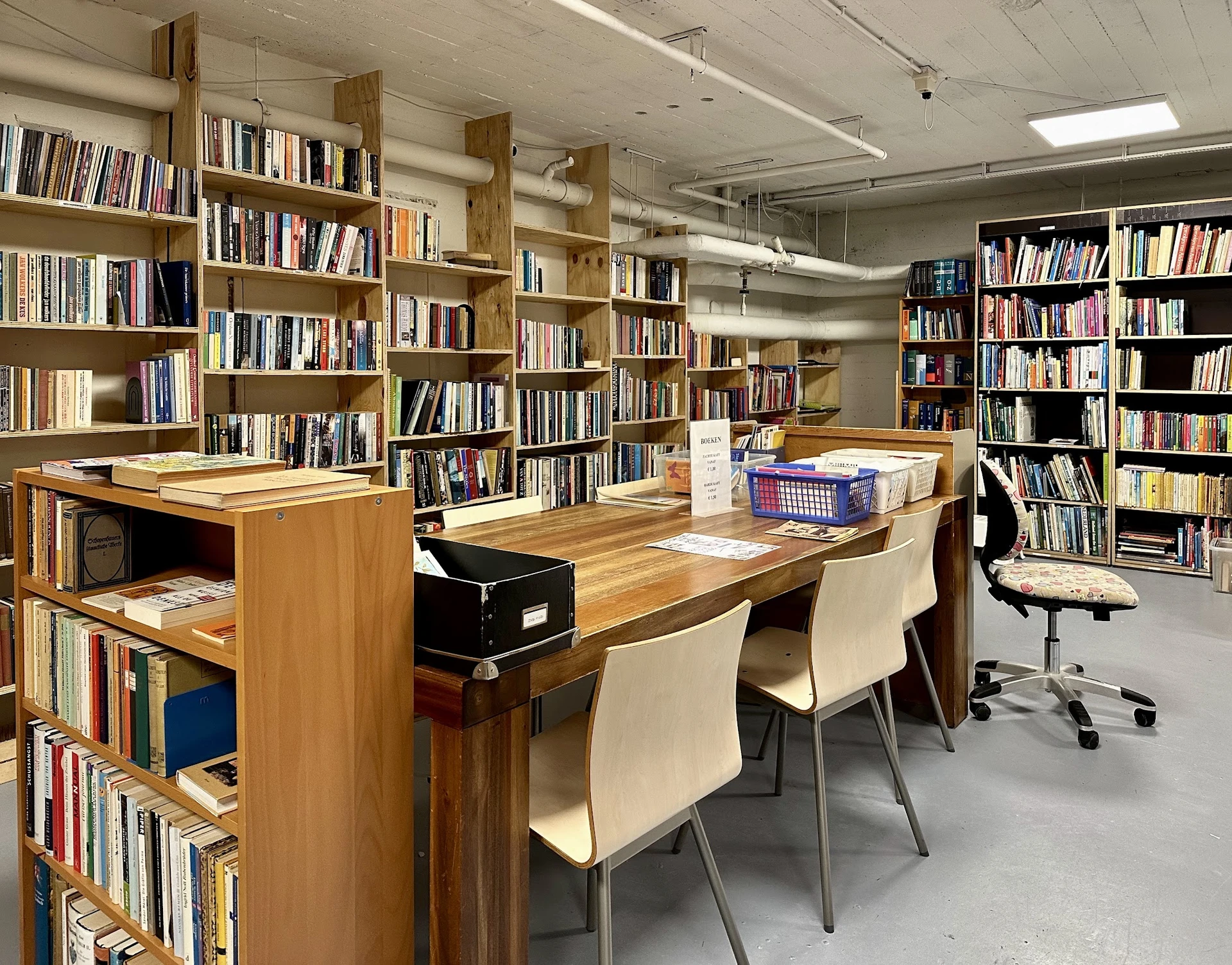 Bibliotheekruimte met houten werkafels, witte stoelen en boekenkasten langs de wanden