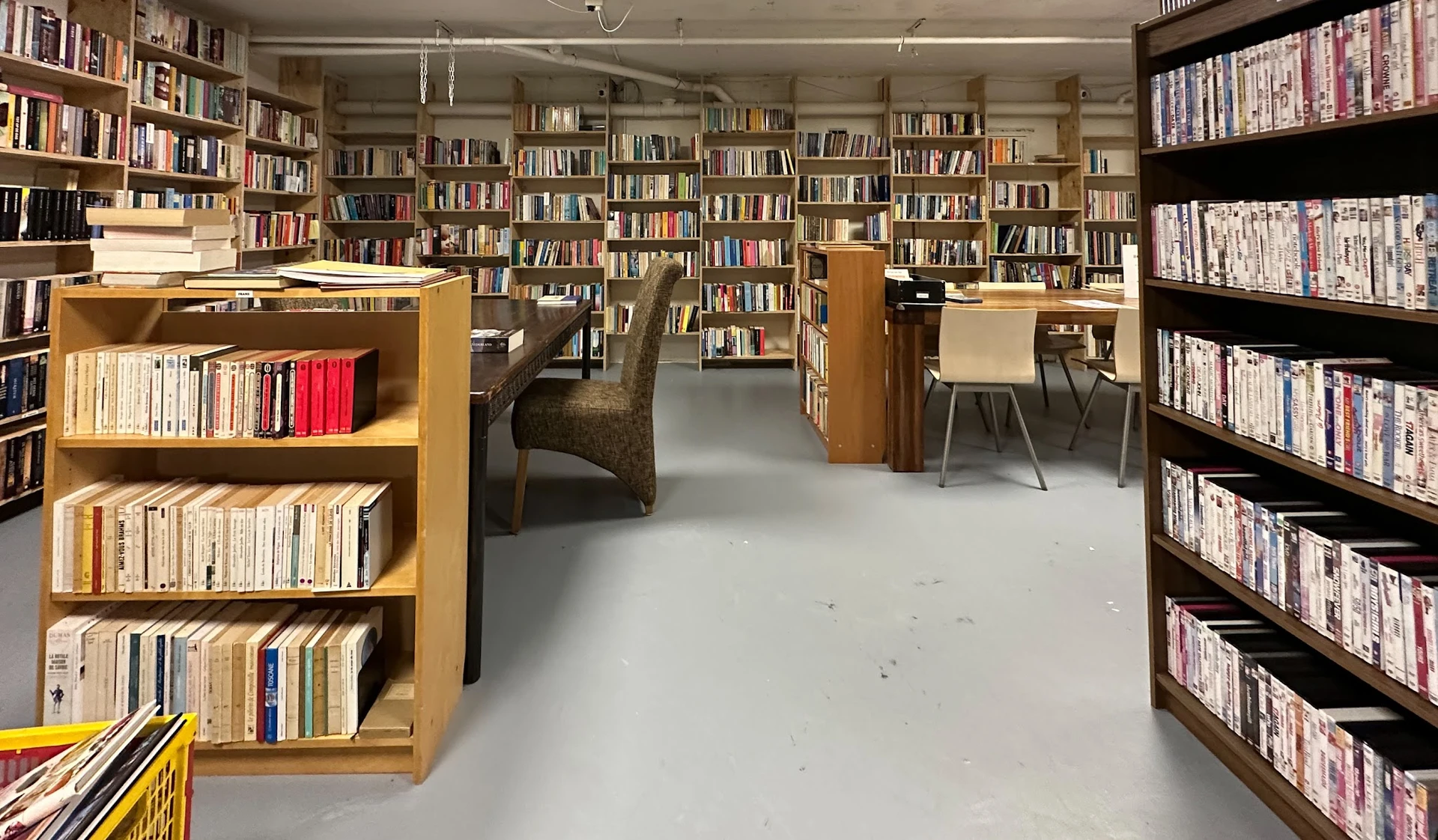 Ruim boekenaanbod in een kringloopwinkel met houten boekenkasten langs de muren en een bruine leunstoel in het midden