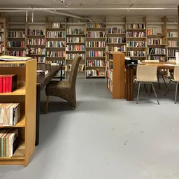 Ruim boekenaanbod in een kringloopwinkel met houten boekenkasten langs de muren en een bruine leunstoel in het midden