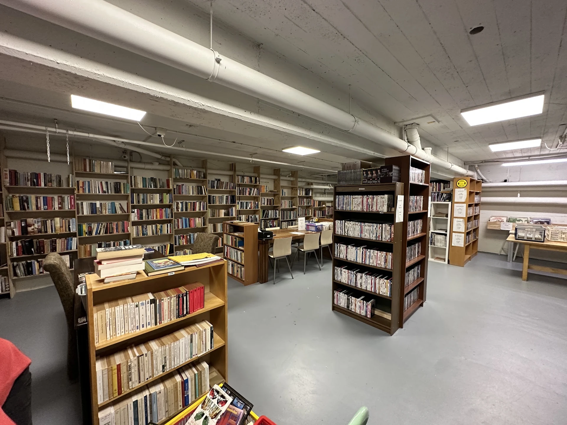 Binnenaanzicht van kringloopwinkel met boekenkasten, stellingen en tafels vol met boeken en media