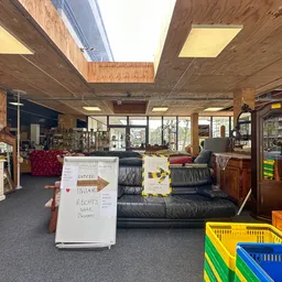 Winkelvloer van kringloopwinkel met zithoek, stellingen, gekleurde kratjes en informatiebord