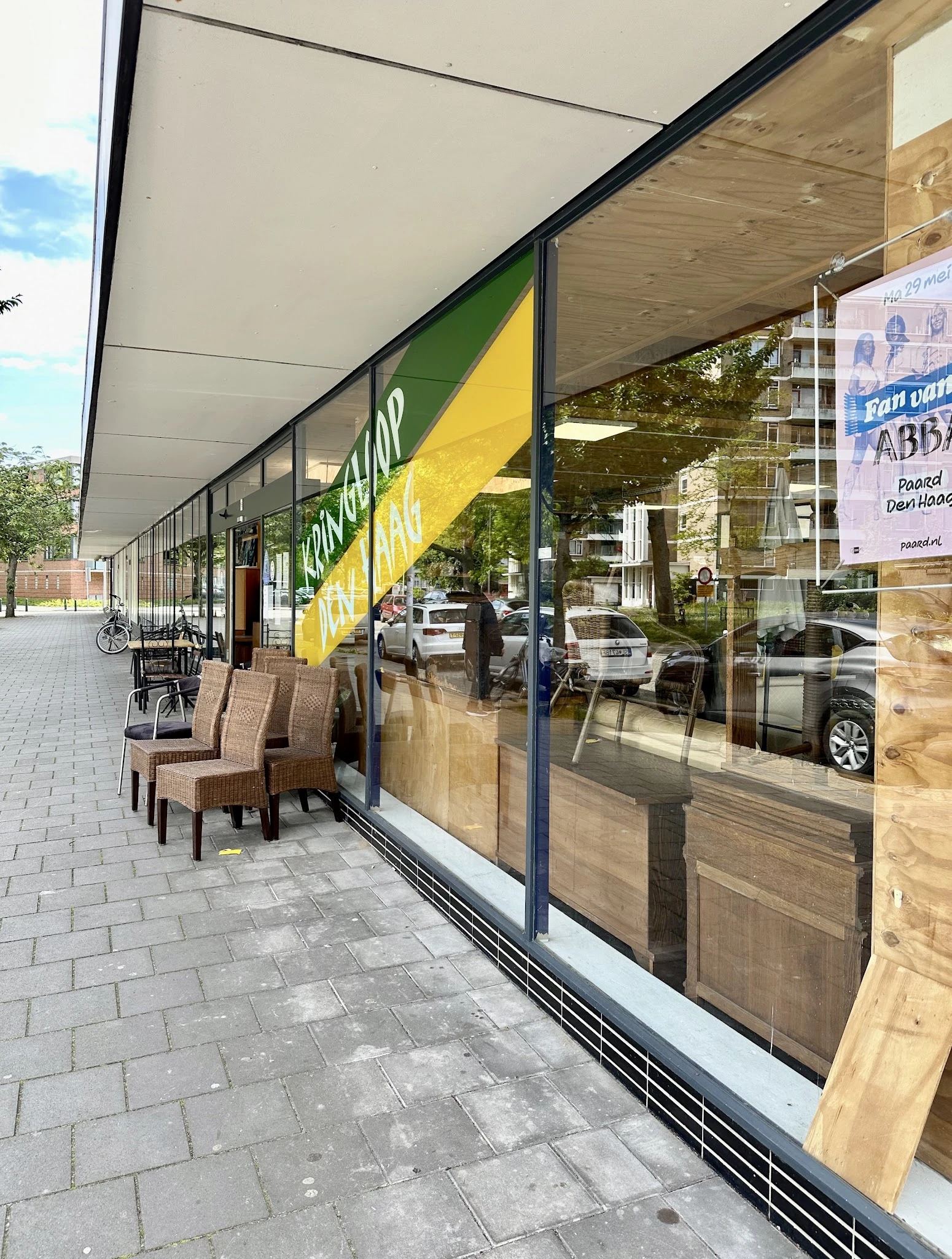 Winkelfront met groengele gevel en grote ramen, enkele stoelen op het terras ervoor