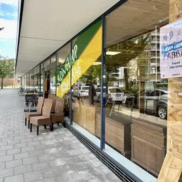 Winkelfront met groengele gevel en grote ramen, enkele stoelen op het terras ervoor