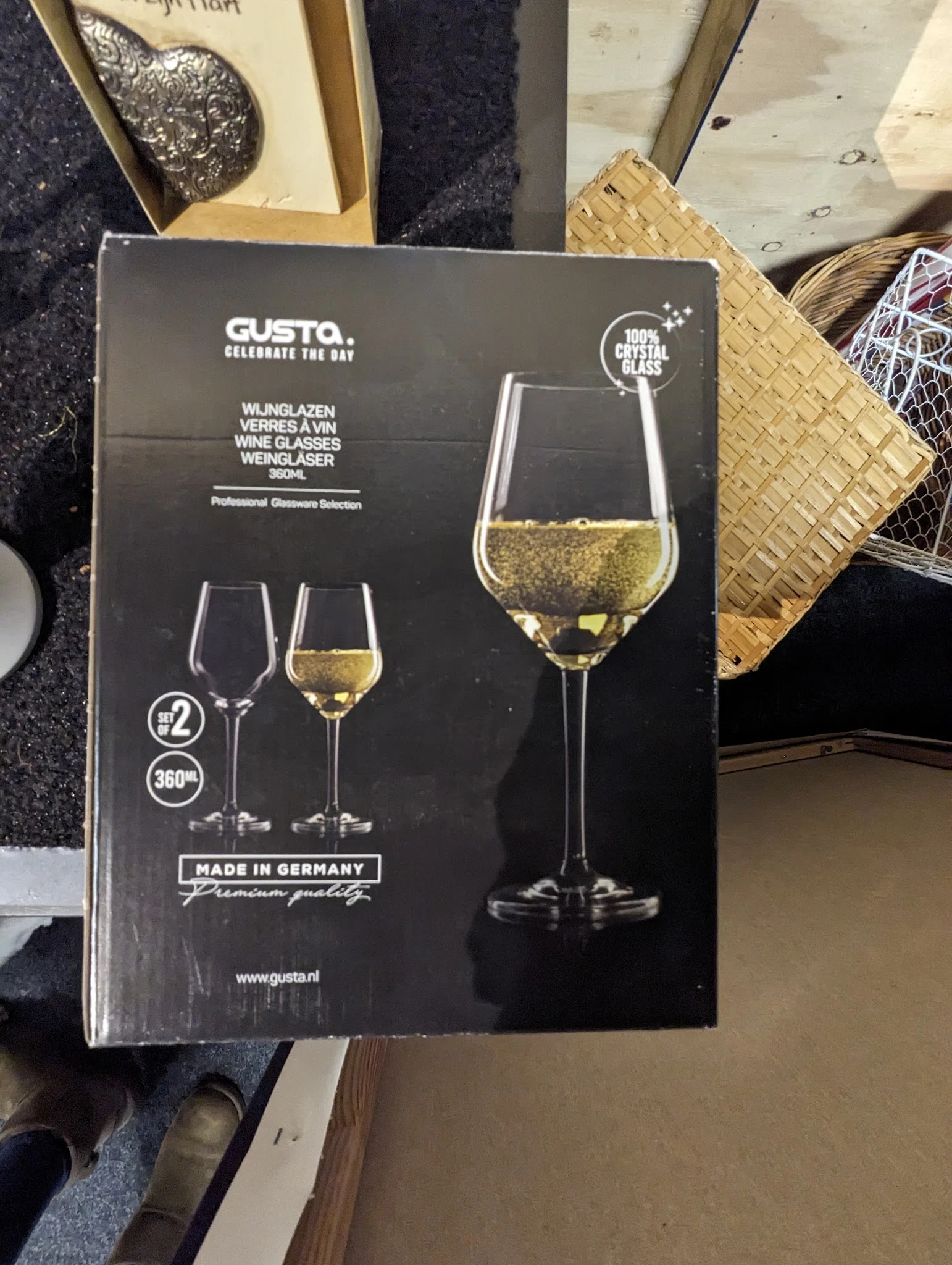 Close-up van een Gusto wijnglasset met twee glazen, één gevuld met witte wijn, op verpakking met Duitse tekst