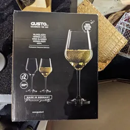 Close-up van een Gusto wijnglasset met twee glazen, één gevuld met witte wijn, op verpakking met Duitse tekst