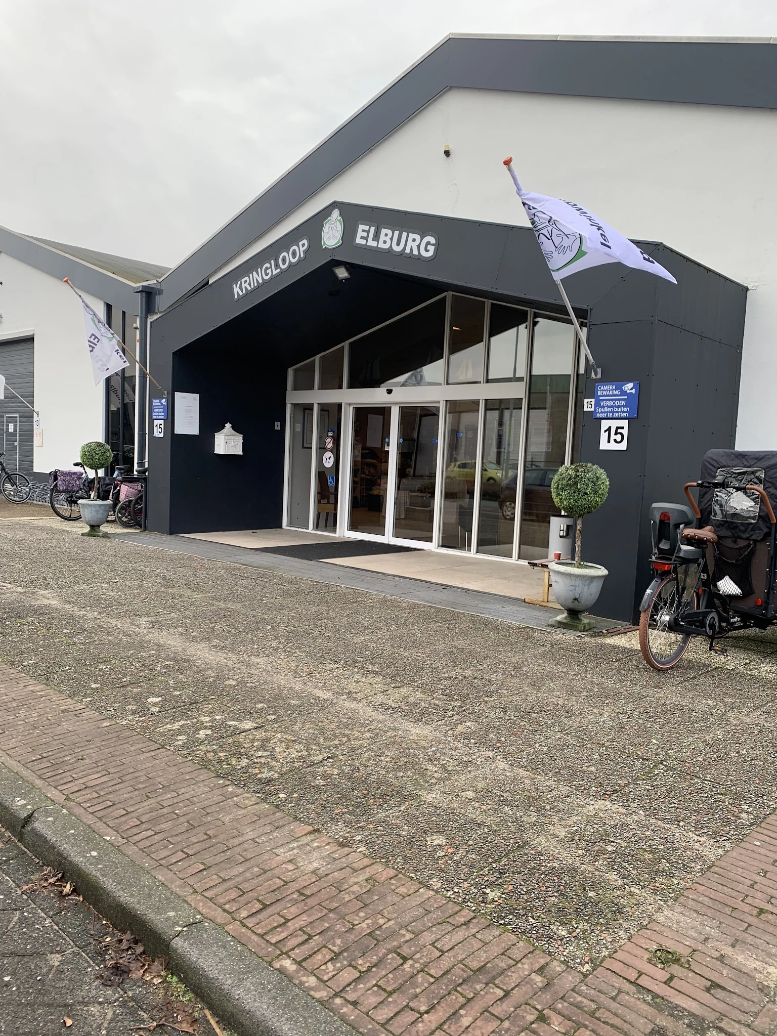 Zwarte gevel van kringloopwinkel met glazen deuren, fietsen en plantenbak ervoor