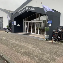 Zwarte gevel van kringloopwinkel met glazen deuren, fietsen en plantenbak ervoor