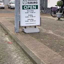 Openingstijden bord met witte standaard op straat: woensdag tot vrijdag 10:00-17:00 uur, zaterdag 10:00-16:30 uur