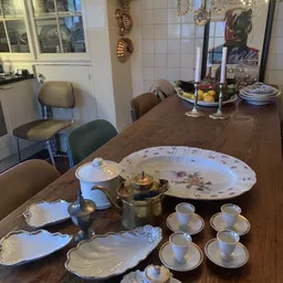 Servies en theepot op houten tafel: borden, kopjes, kannen en decoratieve schalen met bloemmotieven
