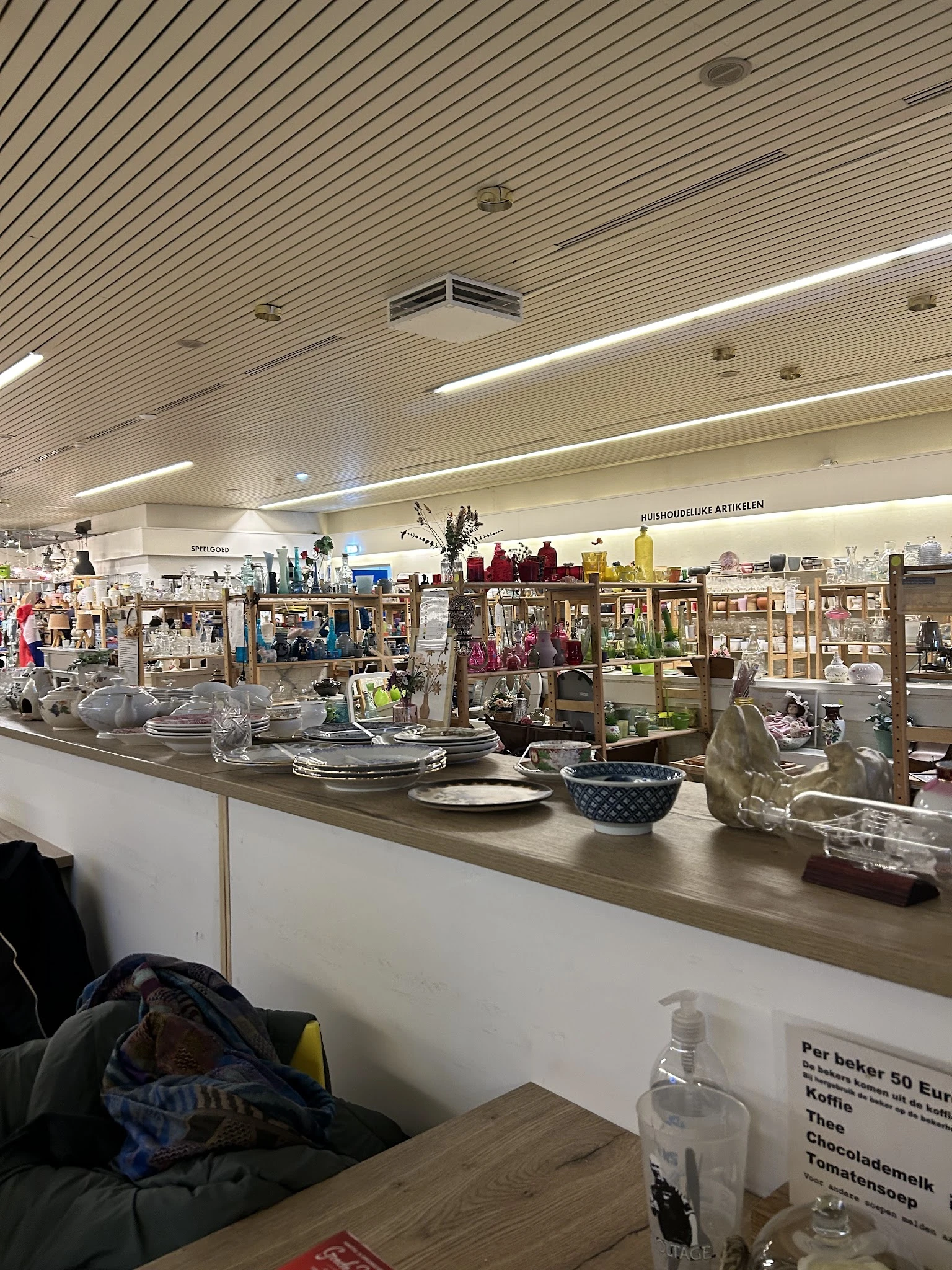 Uitstallingen met huishoudelijke artikelen, servies, decoratie en kitchenware op schappen en toonbank in kringloopwinkel