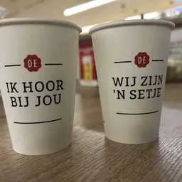 Twee witte koffiebekers met Nederlands opschrift 'Ik hoor bij jou' en 'Wij zijn 'n setje'
