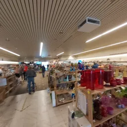 Overzicht van de winkelvloer met verschillende stellingen, artikelen en bezoekers in de kringloopwinkel