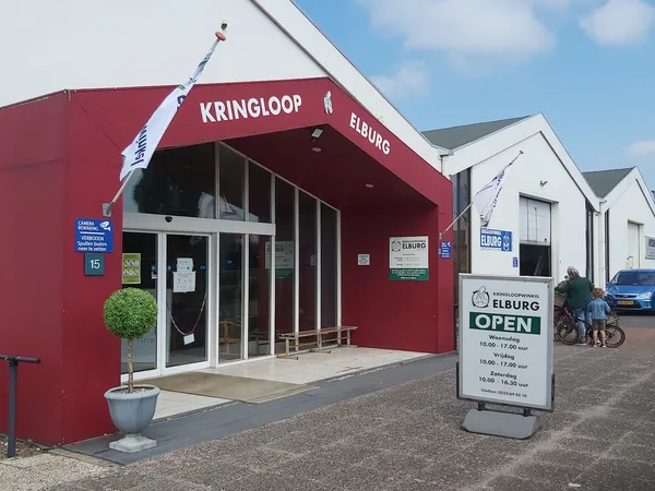 Rode winkelgevel met glazen deuren en ramen, witte zijgebouwen, informatiebord op het terrein