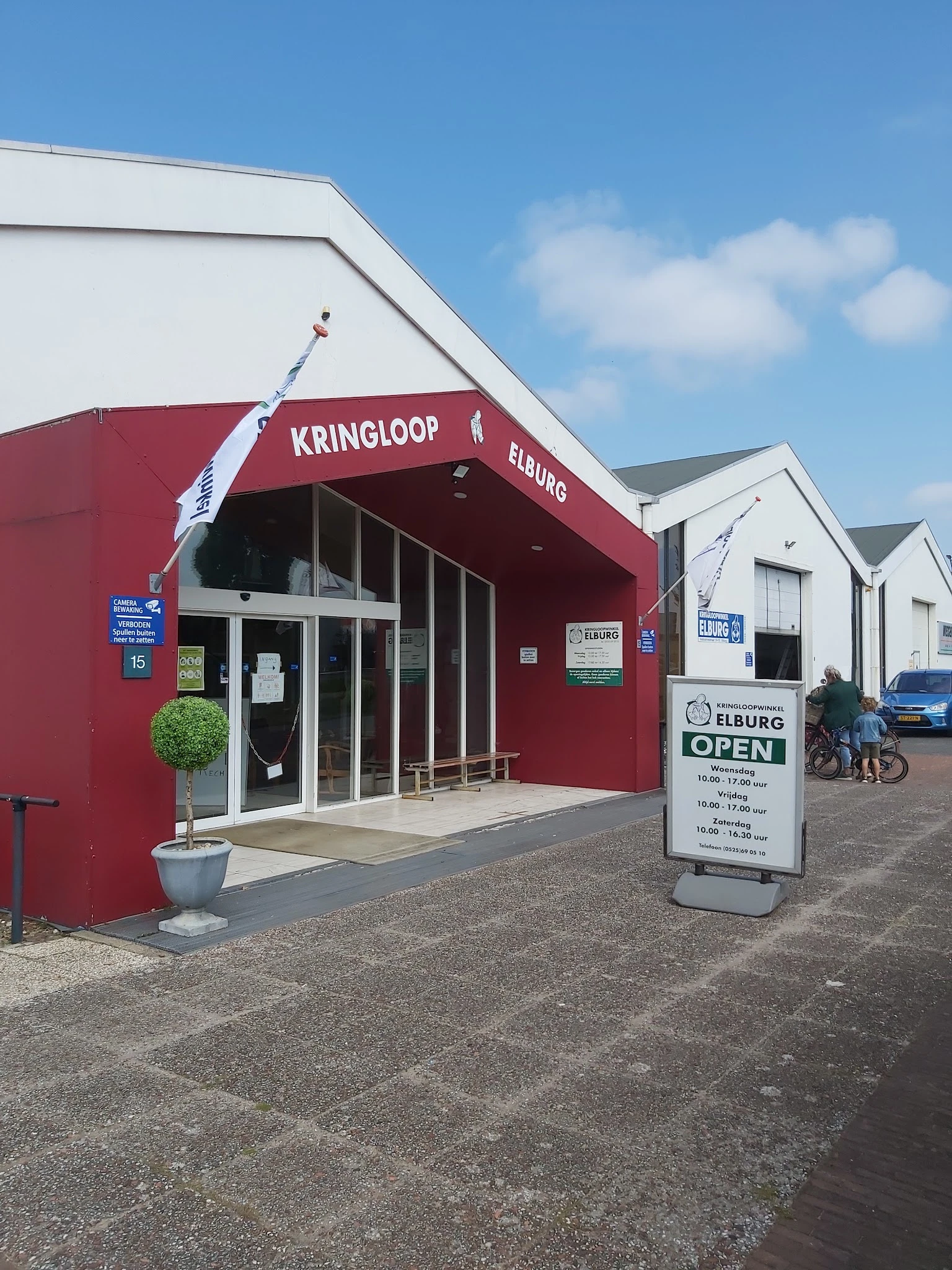 Rode winkelgevel met glazen deuren en ramen, witte zijgebouwen, informatiebord op het terrein