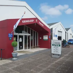 Rode winkelgevel met glazen deuren en ramen, witte zijgebouwen, informatiebord op het terrein
