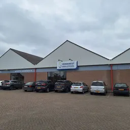 Voorkant van kringloopwinkel Verderest met bakstenen gevel, wit dak en rode kozijnen, parkeerplaats met auto's