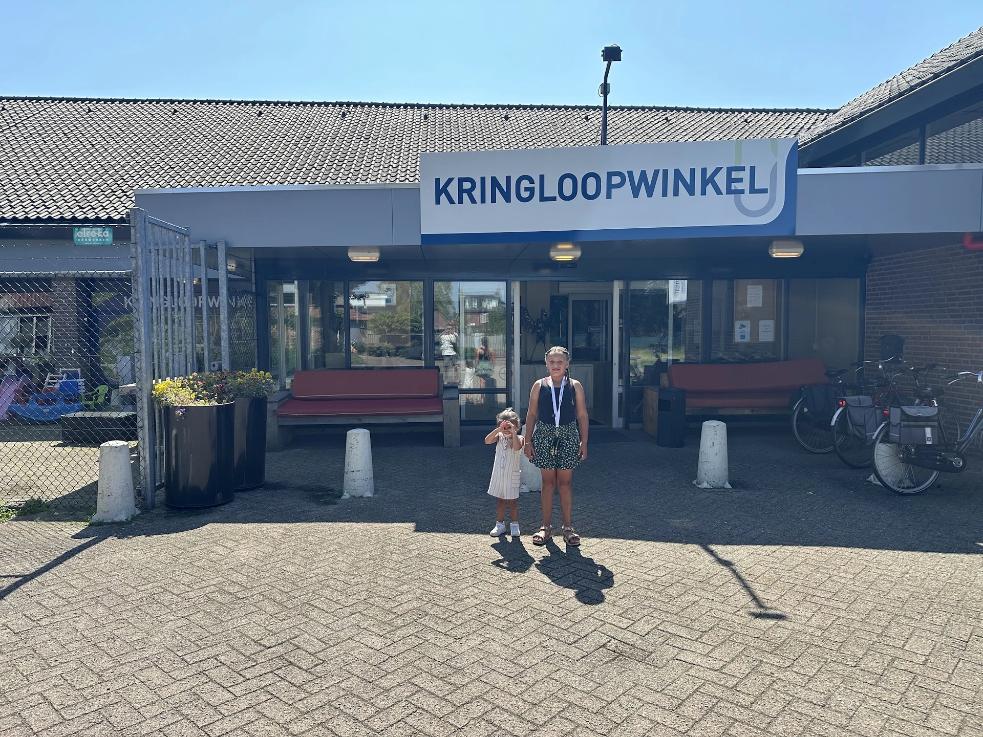 Gevel van kringloopwinkel Verderest met blauwe naam en twee personen ervoor