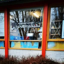 Winkelraam met rode en gele kozijnen, bomen zichtbaar in spiegeling, winkelnaambord op raam