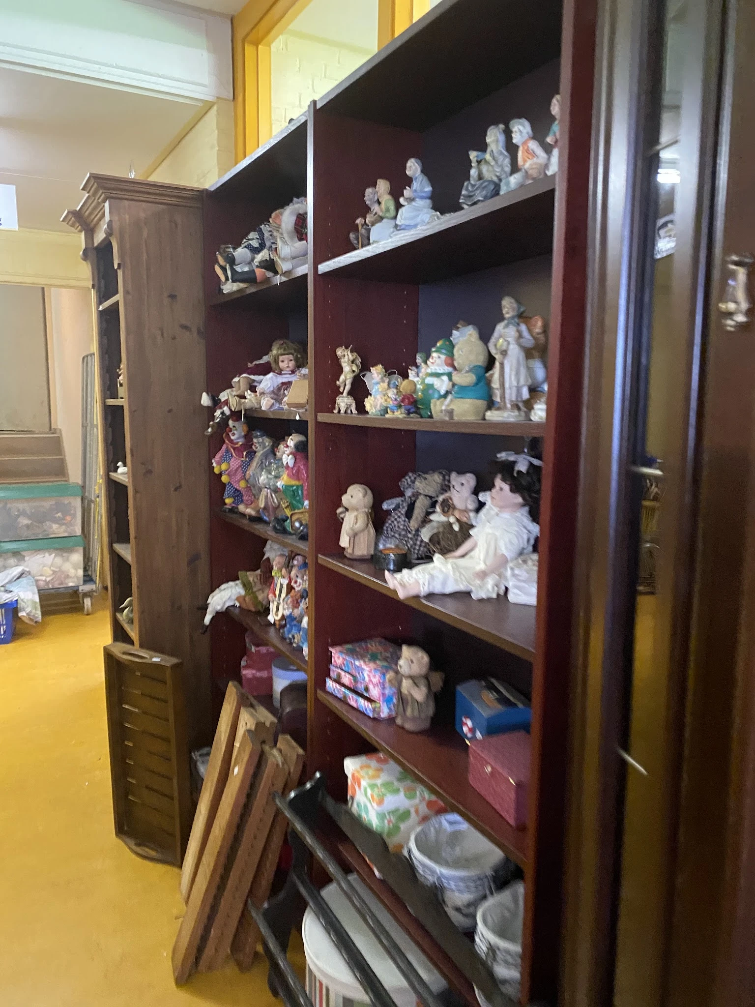 Vitrinekast met verschillende verzamelobjecten: porseleinpoppen, beeldjes en decoratieve artikelen op meerdere niveaus