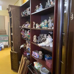 Vitrinekast met verschillende verzamelobjecten: porseleinpoppen, beeldjes en decoratieve artikelen op meerdere niveaus