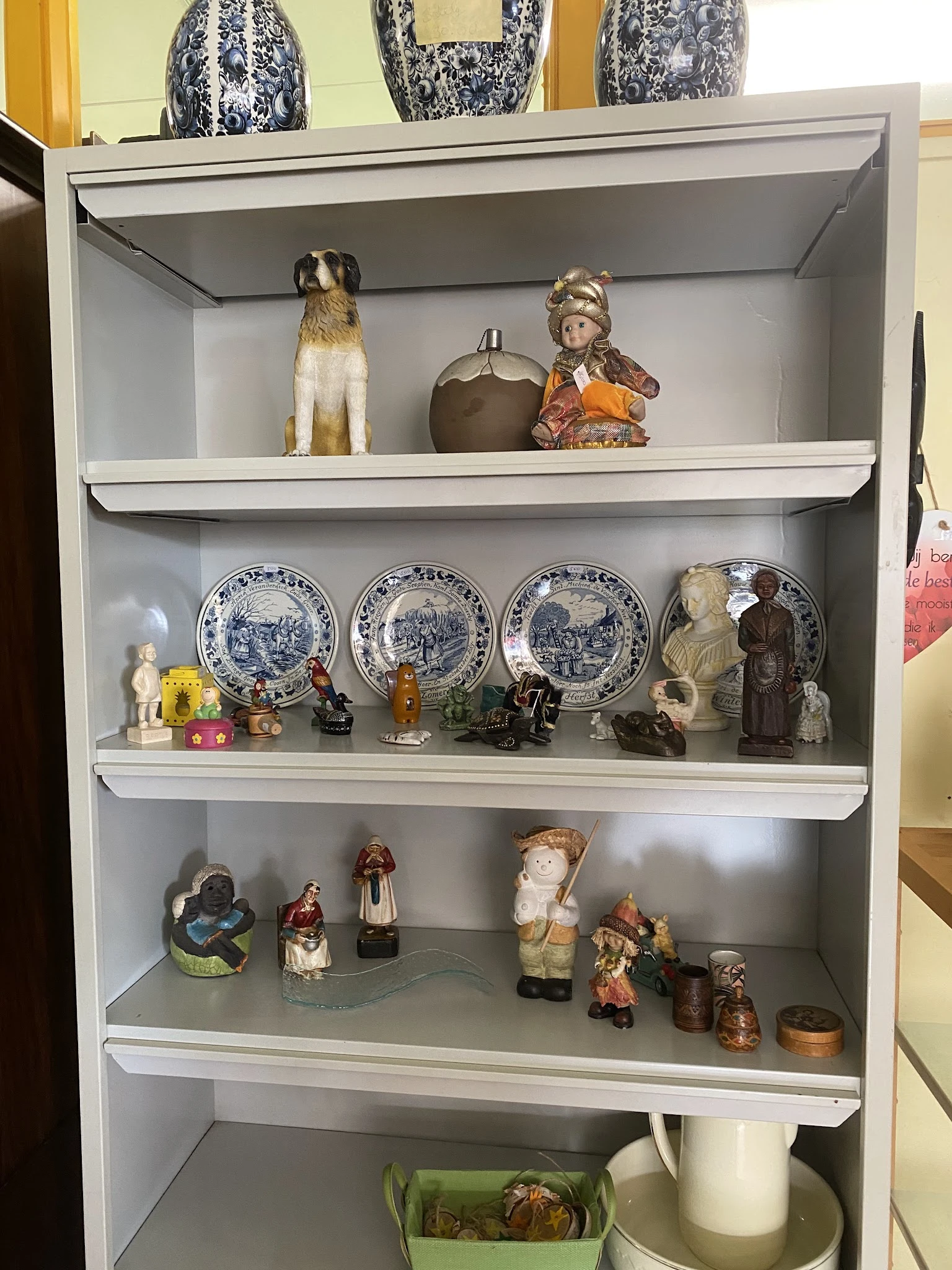 Vitrinekast met decoratieve items: porseleinen borden, beeldjes, vazen en siervoorwerpen netjes uitgestald op drie planken