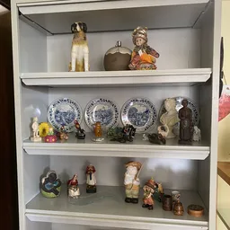 Vitrinekast met decoratieve items: porseleinen borden, beeldjes, vazen en siervoorwerpen netjes uitgestald op drie planken