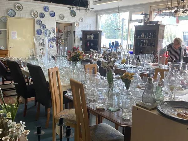 Winkelbinnenruimte met tafels vol kristalglazen, vazen en decoratieartikelen, decoratieve borden aan muur