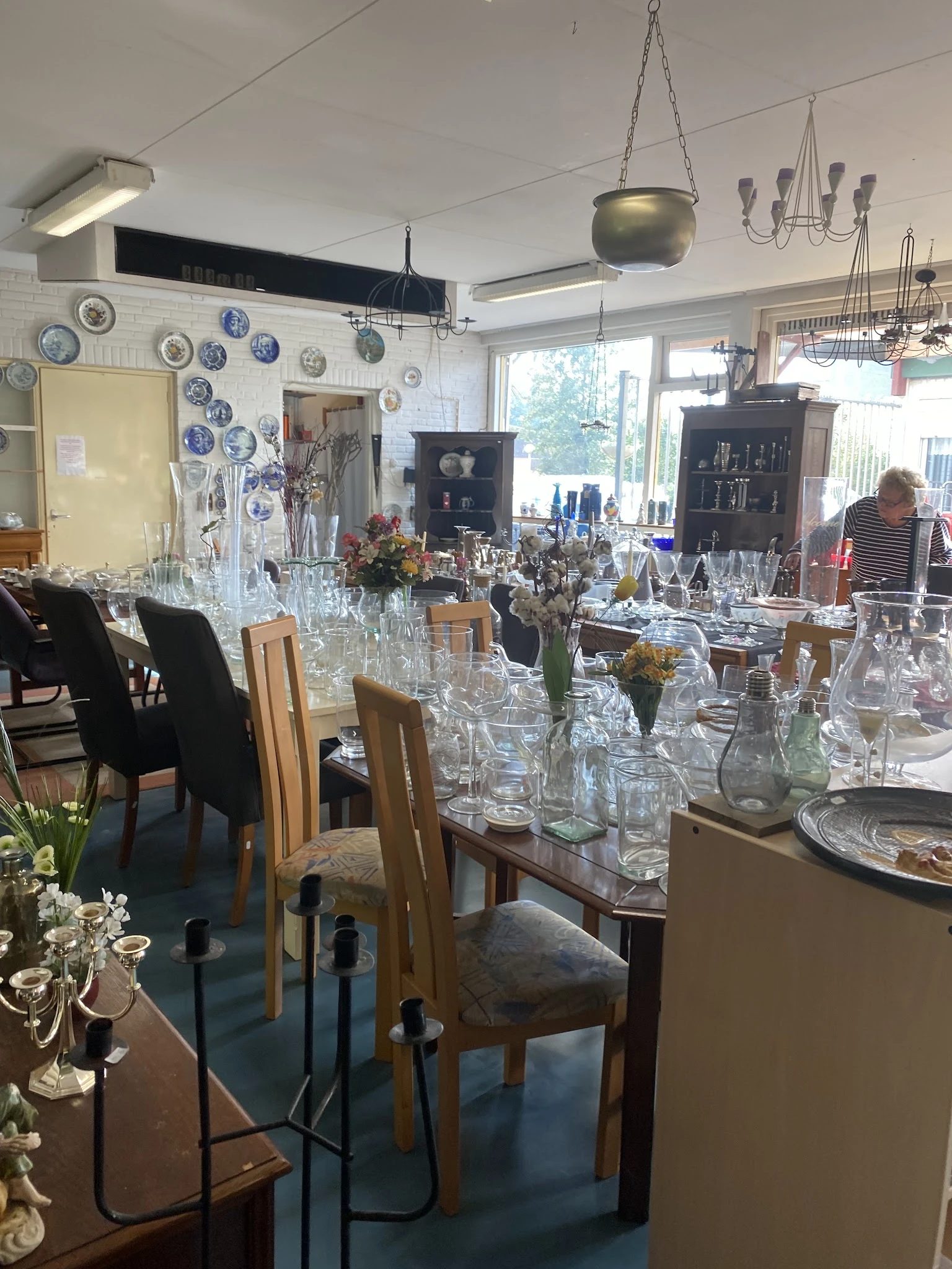 Winkelbinnenruimte met tafels vol kristalglazen, vazen en decoratieartikelen, decoratieve borden aan muur