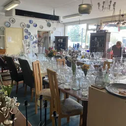Winkelbinnenruimte met tafels vol kristalglazen, vazen en decoratieartikelen, decoratieve borden aan muur