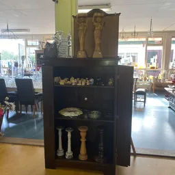 Zwarte vitrinekast met gouden decoratieve beeldjes, schalen en kandelaars op verschillende legels
