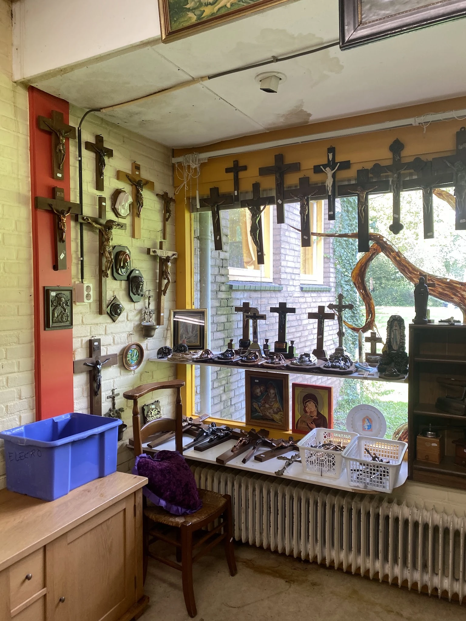 Uitgestalde religieuze artikelen: kruis-wanddecoraties, beeldjes en andere devotionalia in een kringloopwinkel