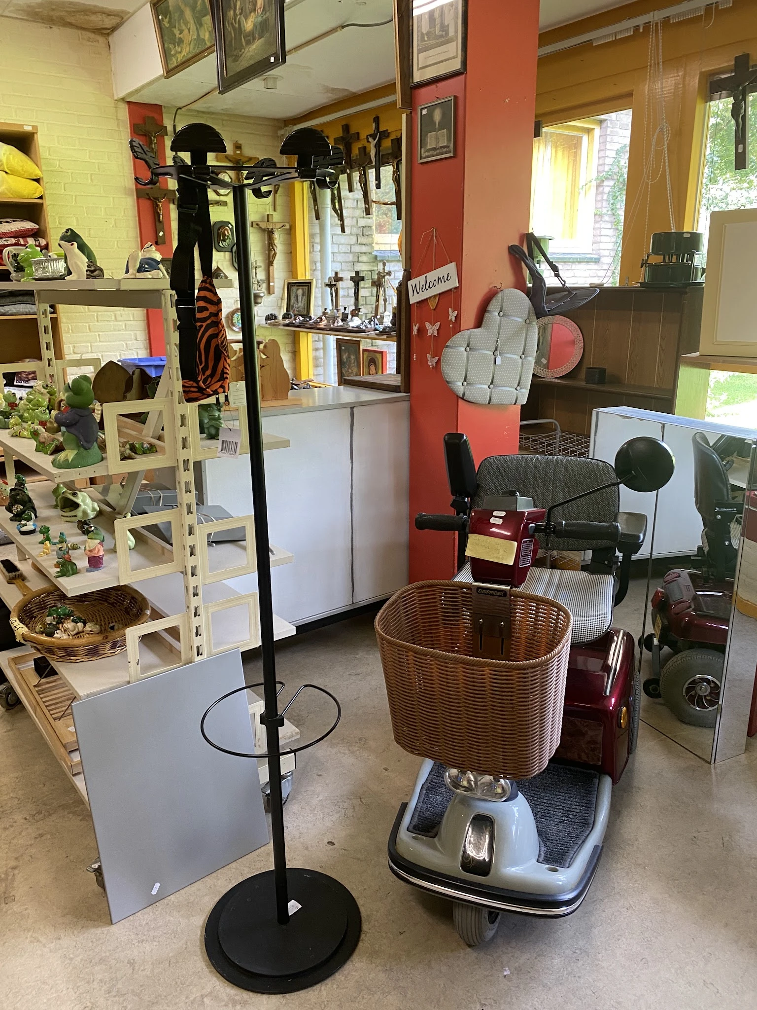Binnenaanzicht van kringloopwinkel met diverse spullen: plantenkast links, elektrische apparaten rechts, mand op de vloer en 