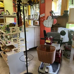 Binnenaanzicht van kringloopwinkel met diverse spullen: plantenkast links, elektrische apparaten rechts, mand op de vloer en 