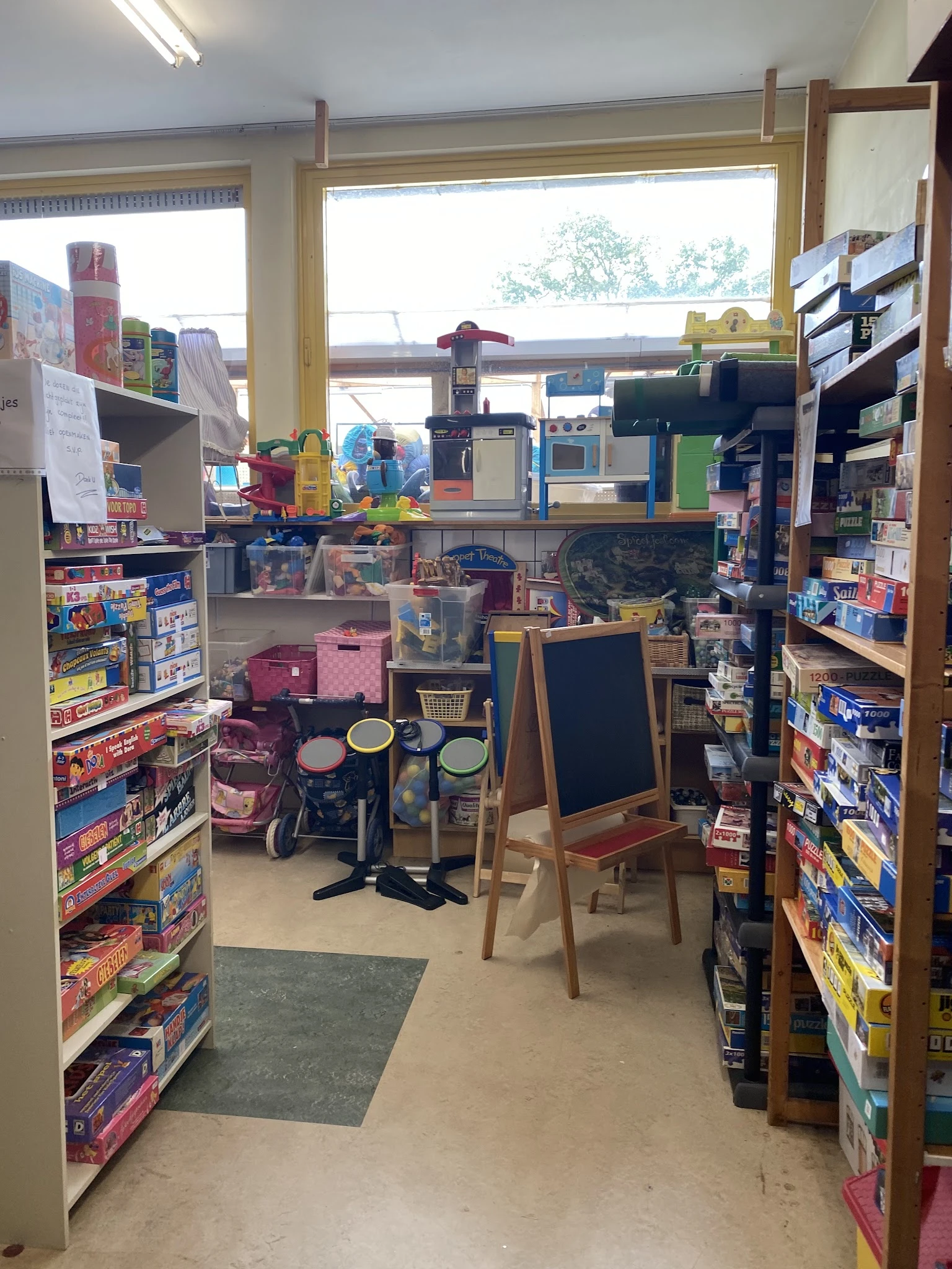 Winkelinterieur met speelgoed, kinderwagens en een krijttafel, omgeven door rekken met producten
