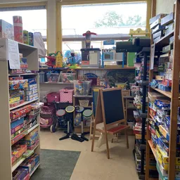 Winkelinterieur met speelgoed, kinderwagens en een krijttafel, omgeven door rekken met producten
