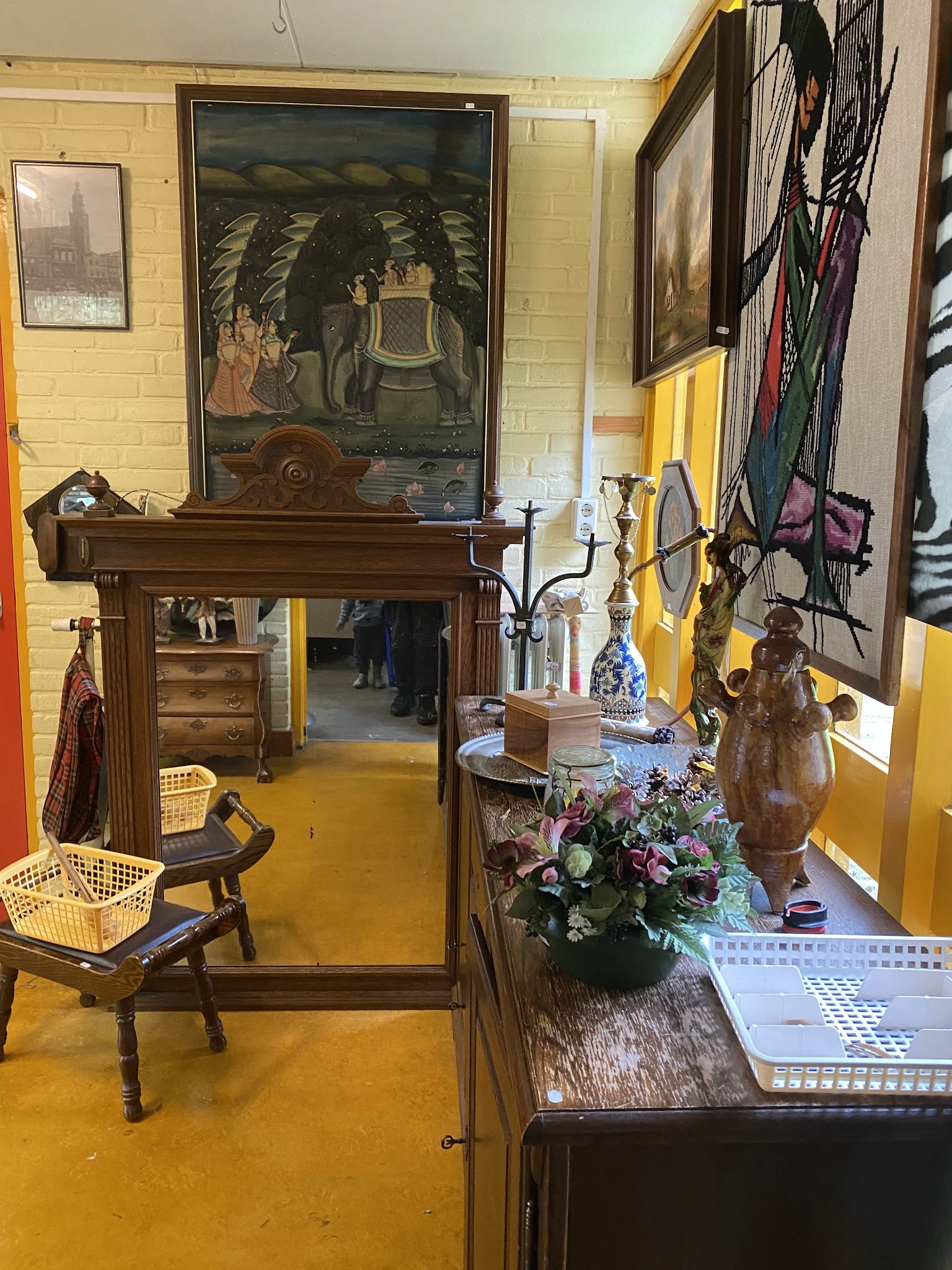 Binnenaanzicht van kringloopwinkel met gele muren, houten meubels, decoratieve objecten en diverse spullen op toonbanken