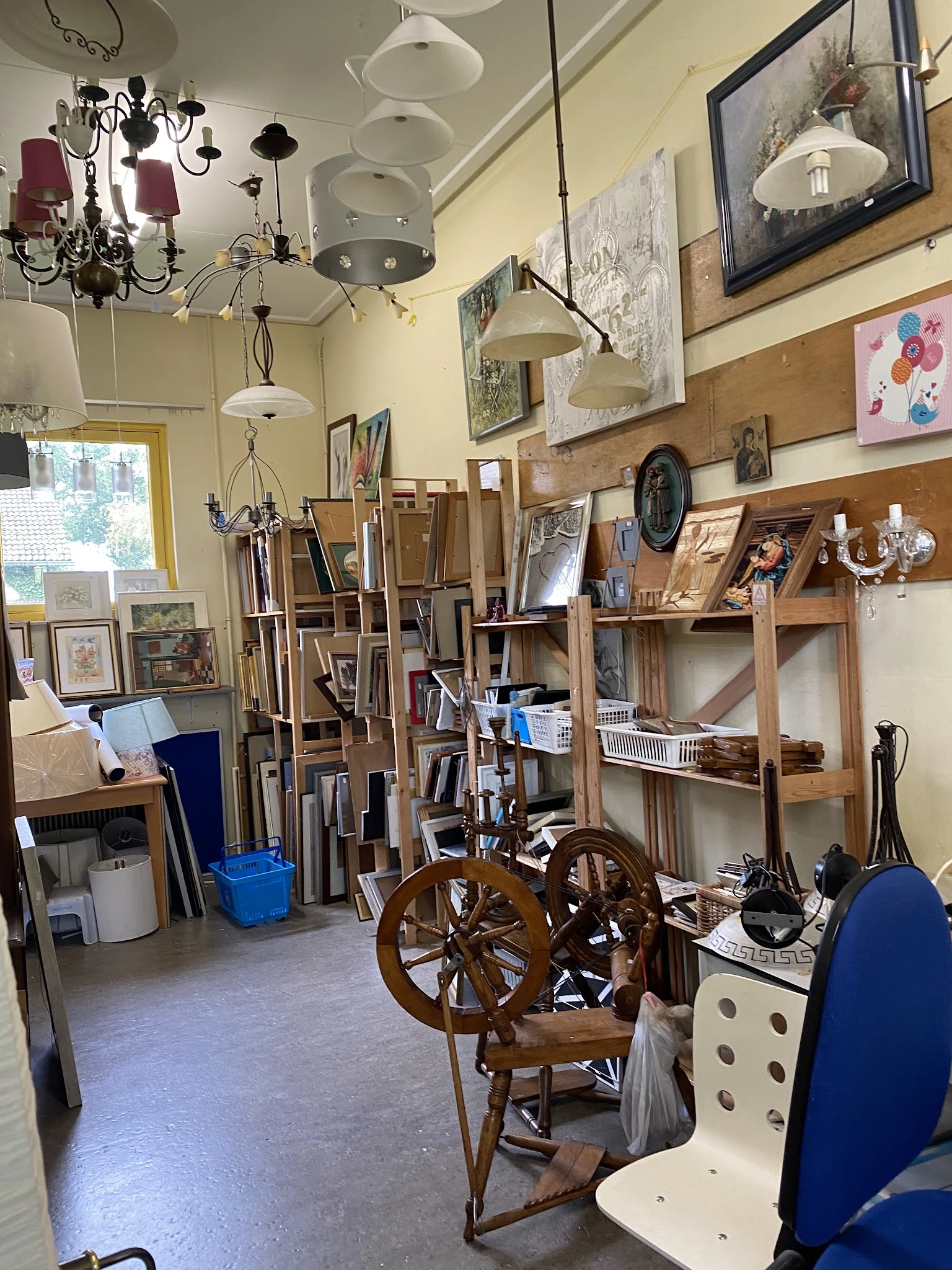 Binnenaanzicht van kringloopwinkel met houten stellingen, kunstwerken, schilderijen, antieke wielen en diverse tweedehandsart