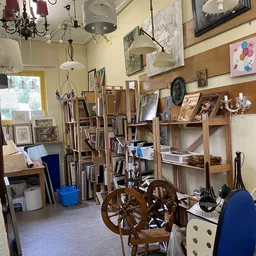 Binnenaanzicht van kringloopwinkel met houten stellingen, kunstwerken, schilderijen, antieke wielen en diverse tweedehandsart