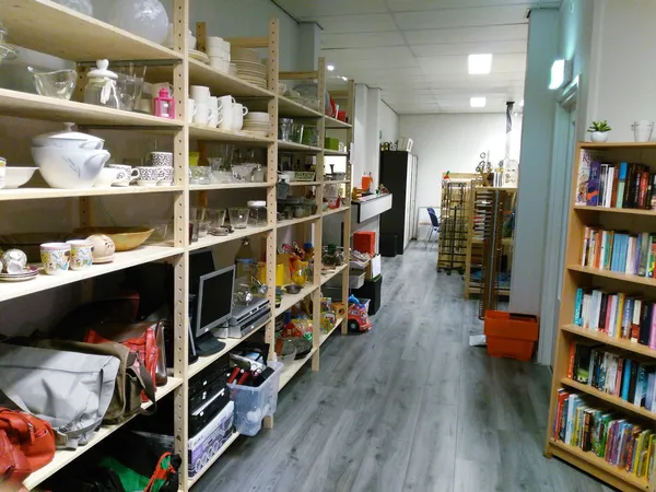Winkelinterieur met houten stellingen vol huishoudgoederen, boeken in kasten, houten vloer en helder verlicht