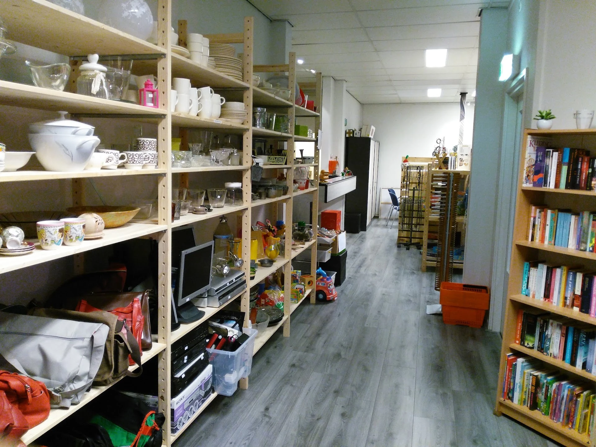 Winkelinterieur met houten stellingen vol huishoudgoederen, boeken in kasten, houten vloer en helder verlicht