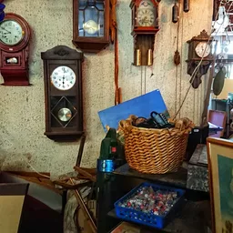 Binnenkant van kringloopwinkel met verschillende wandklokken, een mand met spullen en assortiment huishoudelijke artikelen