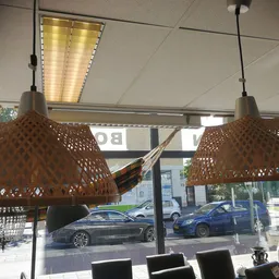 Interieur van kringloopwinkel met twee bruine hangende lampen boven zwarte stoelen, uitzicht op straat met geparkeerde auto's