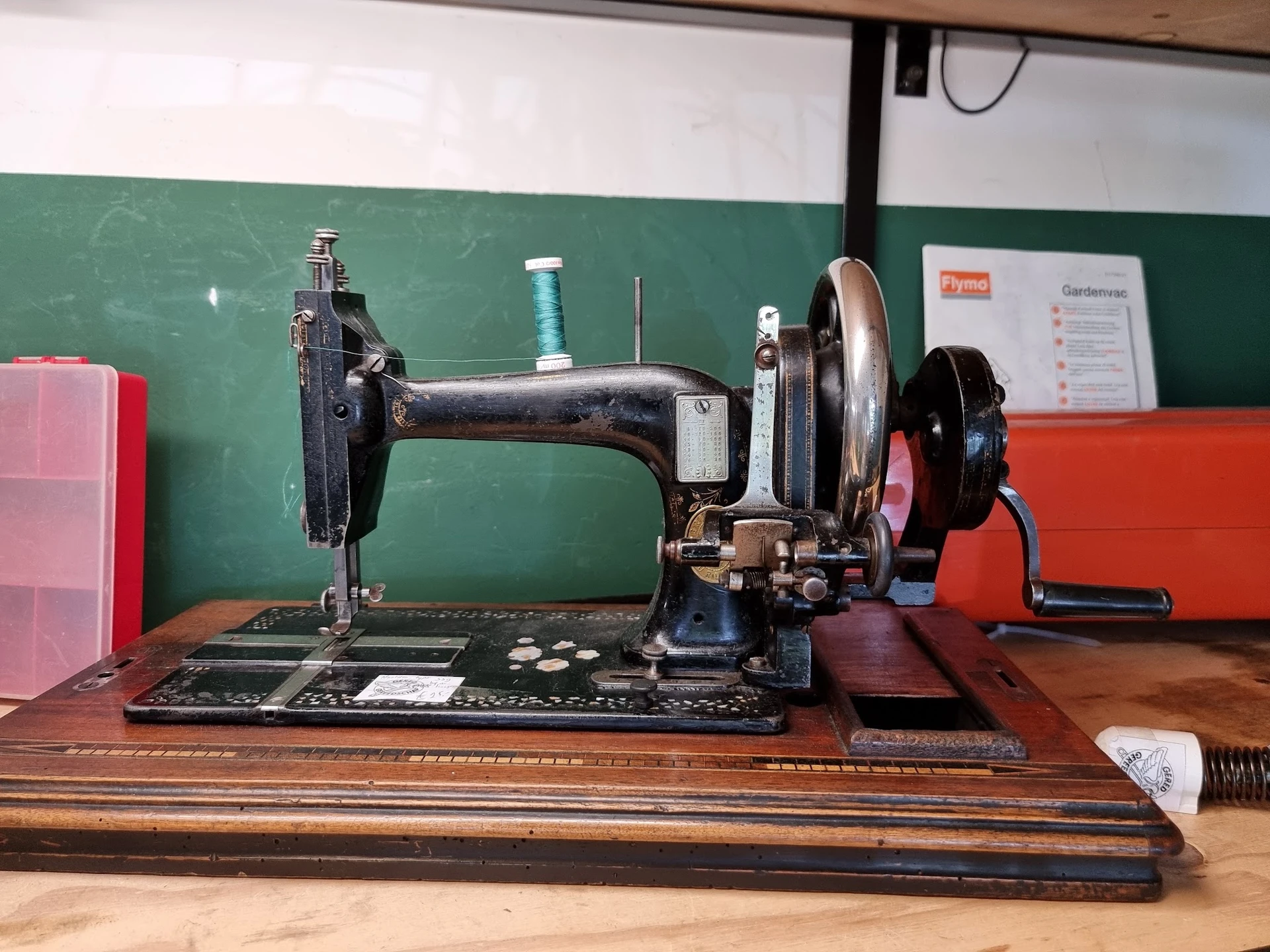 Antieke naaimachine in zwart metaal op houten voet, uitgestald op groene muur