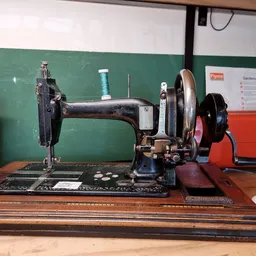 Antieke naaimachine in zwart metaal op houten voet, uitgestald op groene muur