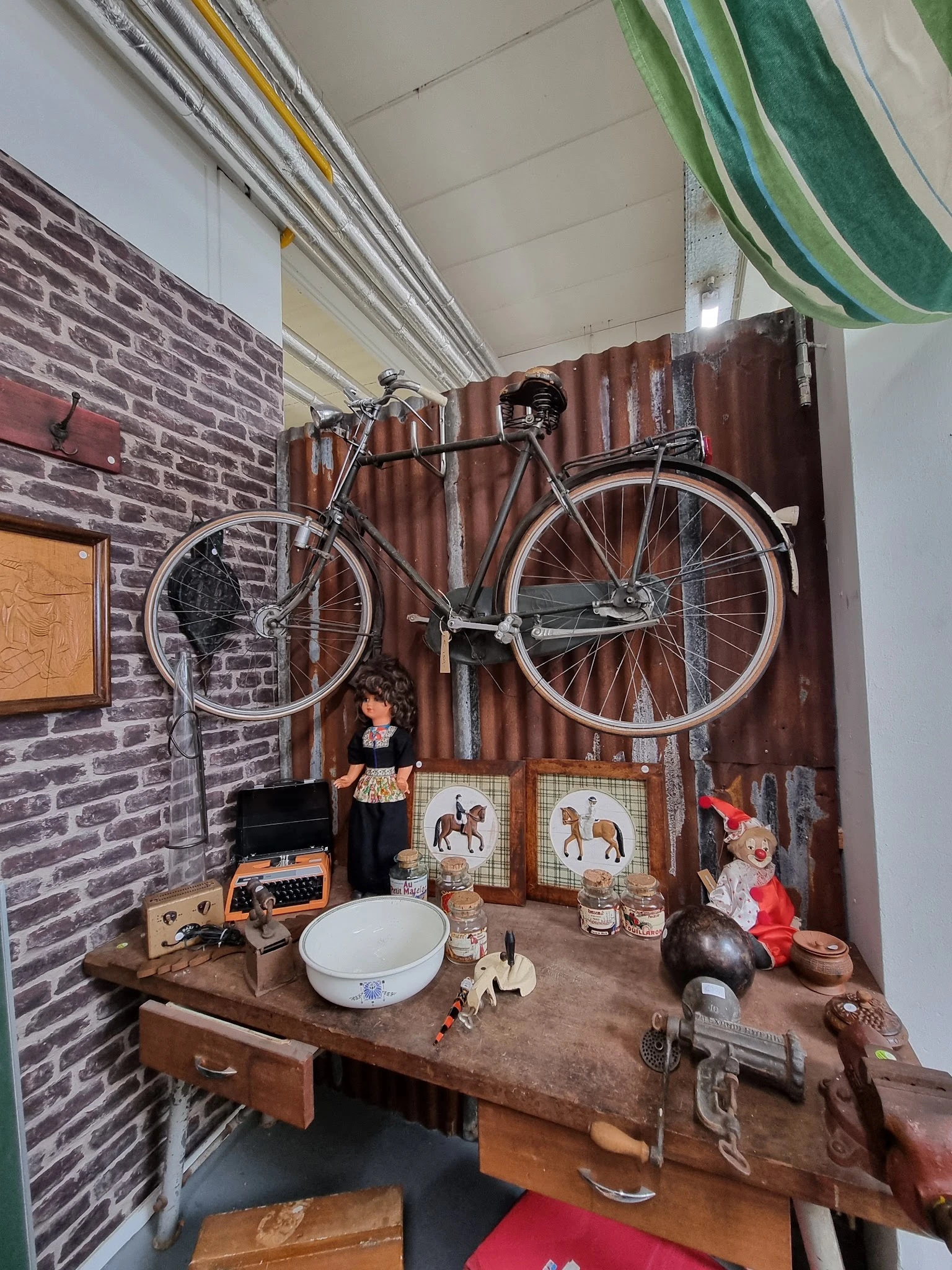 Winkelvloer met bakstenen wand, fiets hangend aan muur, tafeltje met diverse tweedehandsartikelen en decorstukken