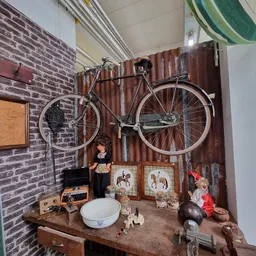 Winkelvloer met bakstenen wand, fiets hangend aan muur, tafeltje met diverse tweedehandsartikelen en decorstukken