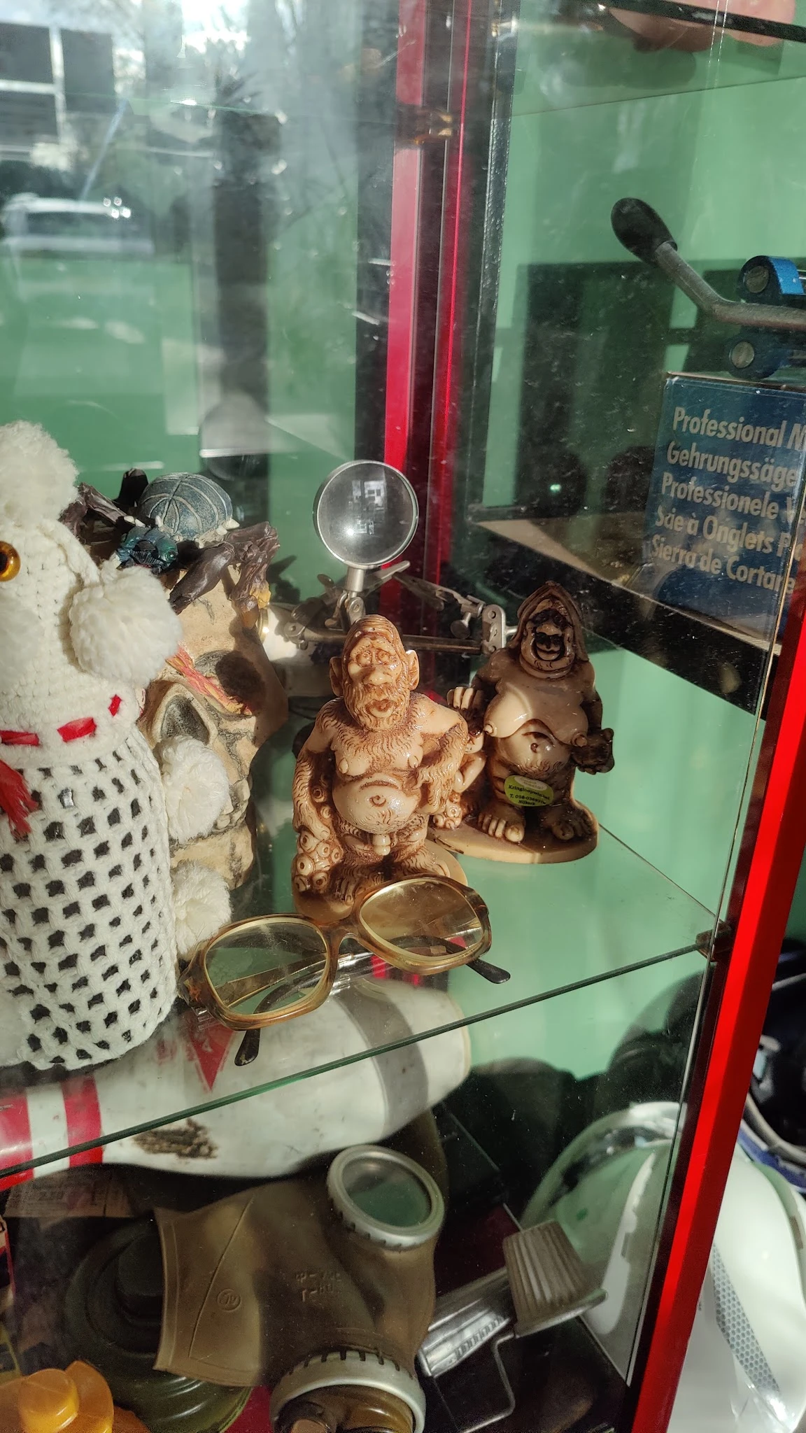 Vitrine met diverse tweedehands items: decoratieve houten beeldjes, schedel, bril en andere curiosa
