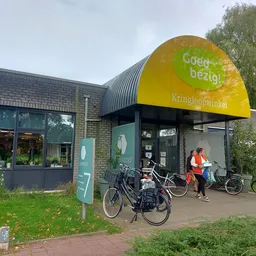 Voorkant van kringloopwinkel met gele luifel, bakstenen gevel en fietsen ervoor geparkeerd