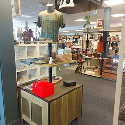 Winkelvloer met stellingen vol spullen, kleding aan hangers en een rode doos op een tafel
