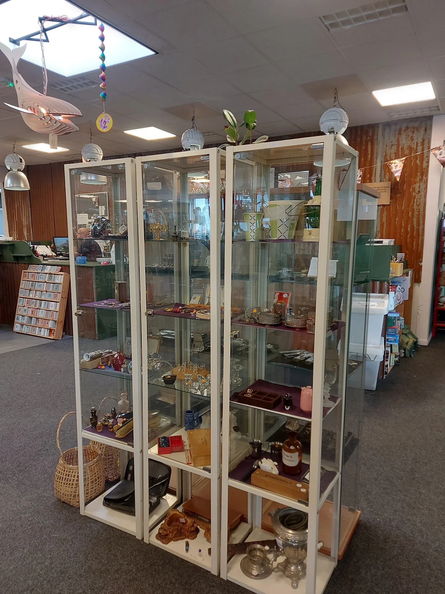 Glazen vitrinekasten met diverse tweedehands artikelen, waaronder porselein, decoratieve voorwerpen en andere huishoudelijke 
